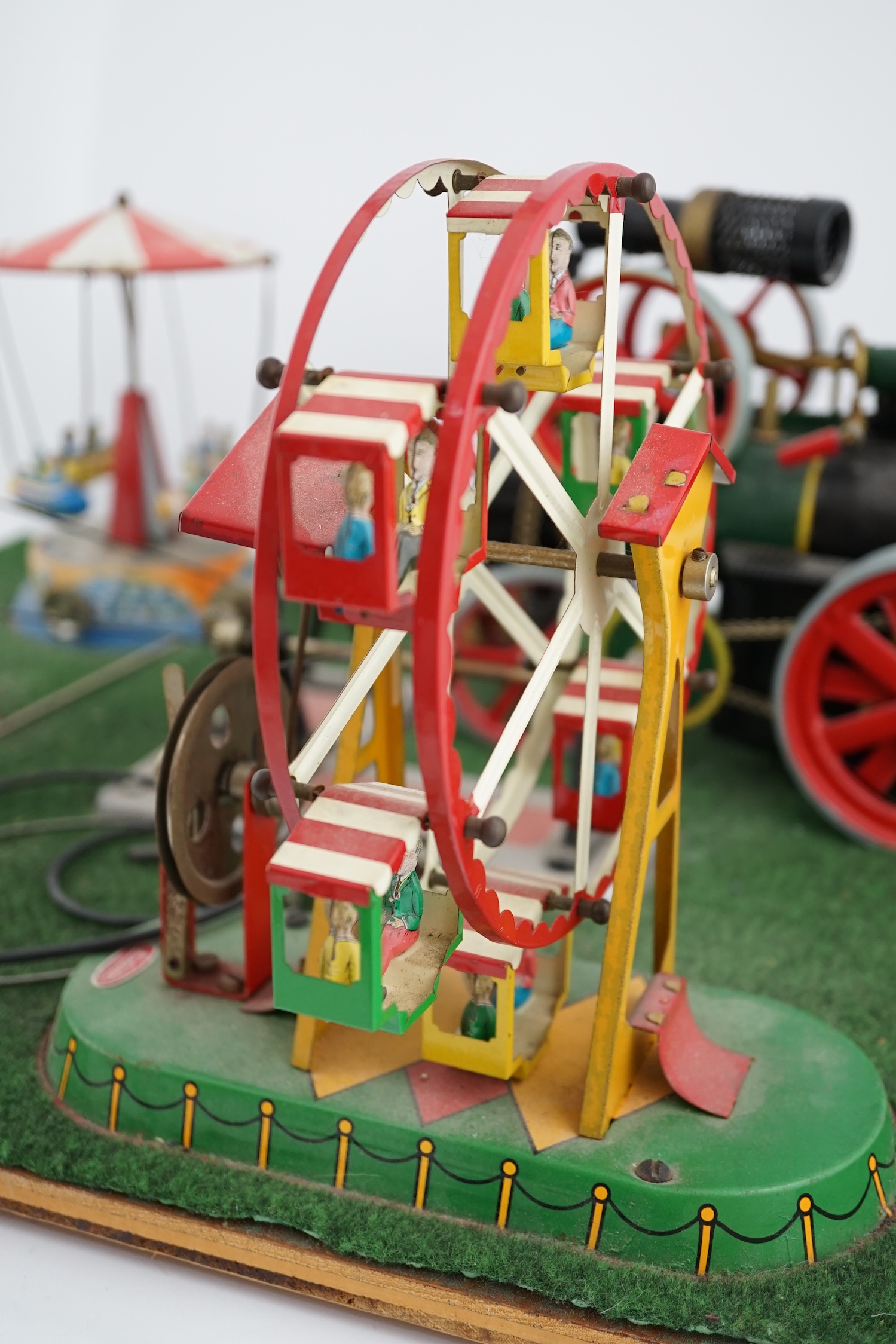 A Wilesco live steam fairground diorama, comprising a D430 pellet fired traction engine, powering a pulley and gear assembly, in turn running three tinplate fairground rides, mounted on a plywood sheet topped with grass